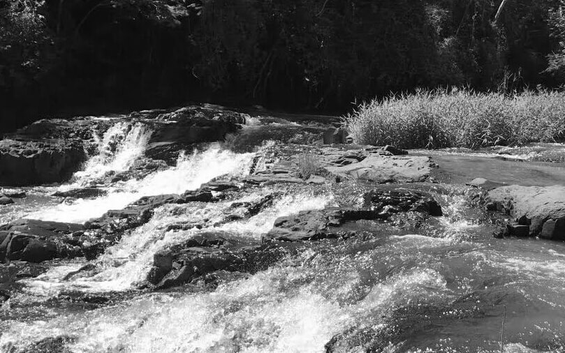 Imagem em preto e branco mostra o Rio Paranapanema. Há pedras e sobre elas passa água em correnteza.